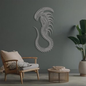 May include: A gray alien creature wall decor with a detailed design. The alien is depicted in a curled position with its tail wrapped around its body. The decor is mounted on a gray wall.