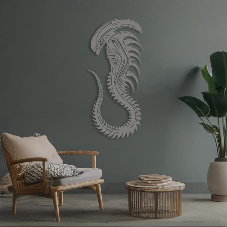 May include: A gray alien creature wall decor with a detailed design. The alien is depicted in a curled position with its tail wrapped around its body. The decor is mounted on a gray wall.