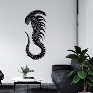 May include: Black alien creature wall decal with a detailed design. The decal is mounted on a white wall in a living room setting.