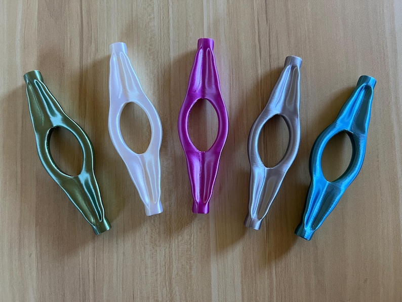 May include: Five different coloured bookmark holders. The holders are made of plastic and have a unique shape. The colours are green, white, pink, grey, and blue.