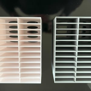 May include: Two white plastic storage organizers with multiple compartments. The organizer on the left has a slightly off-white color and the organizer on the right is a darker shade of white.