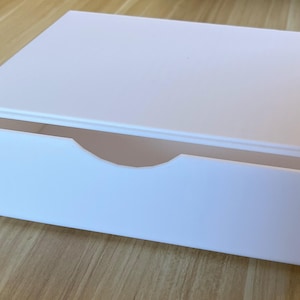 May include: A white ceramic mug with a black handle and the text "But First, Coffee" in a black, handwritten-style font. The mug is on a white surface.