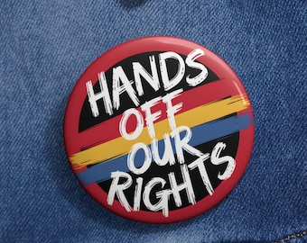 May include: A red, yellow, and blue button with the text "Hands Off Our Rights" in black lettering.