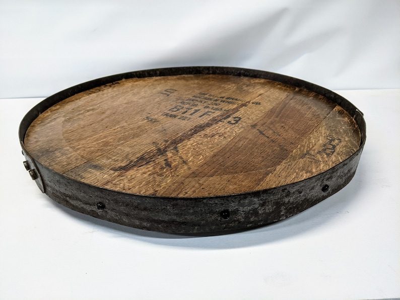 May include: A round wooden tray with a metal rim and a metal band around the edge. The wood has a dark brown stain and the metal is a rusty brown colour. The tray has a label on the top that reads "B11F3".