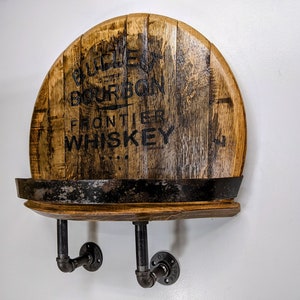 Op de afbeelding: Een houten plank gemaakt van een hergebruikt whiskeyvat met zwarte metalen pijpbeugels. Het vat is gelabeld met "Old Frontier Bourbon Whiskey".
