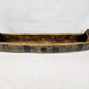 K&ouml;nnte beinhalten: Ein Holz-Pflanzgef&auml;&szlig; aus einem wiederverwendeten Whiskyfass. Der Pflanzkasten ist braun und schwarz mit einer nat&uuml;rlichen Holzoptik. Er hat eine geschwungene Form und ist perfekt f&uuml;r die Pr&auml;sentation von Pflanzen oder Blumen.
