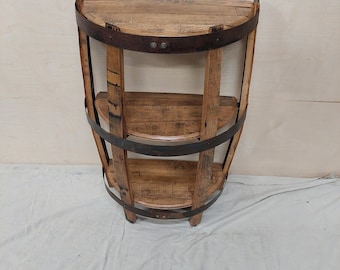 May include: A half-barrel shelf unit made of wood with three shelves and metal bands. The shelf unit is stained a light brown color and has a rustic look.