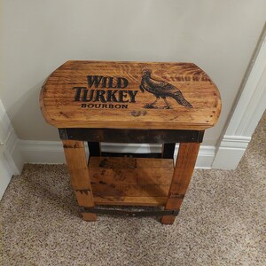 May include: A wooden stool with a Wild Turkey Bourbon barrel top. The top is stained brown and features the Wild Turkey logo and a turkey illustration.