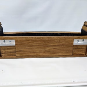 May include: A wooden planter box made from reclaimed oak barrel staves. The planter has a dark brown stain and two metal brackets on the sides.
