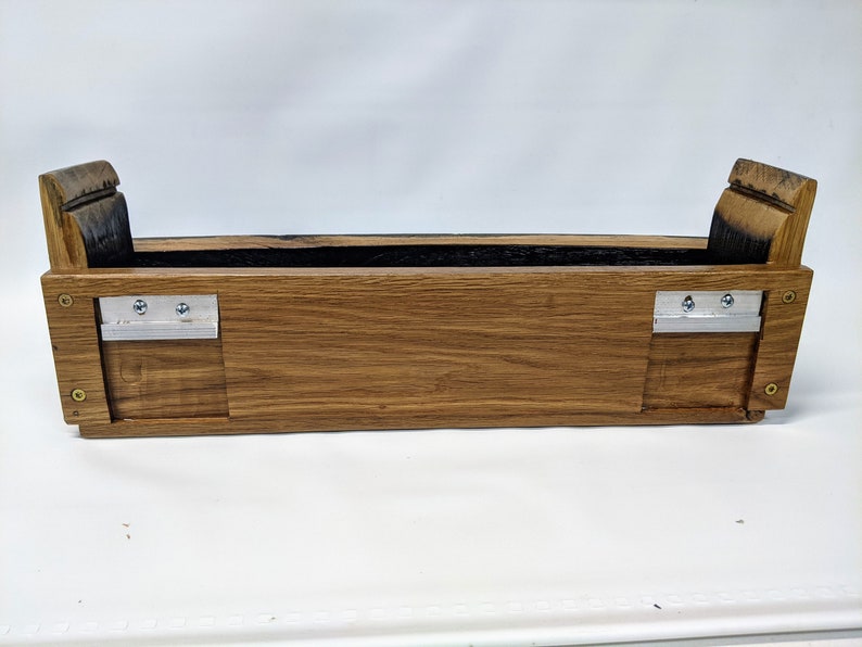 May include: A wooden planter box made from reclaimed oak barrel staves. The planter has a dark brown stain and two metal brackets on the sides.