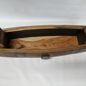 May include: A wooden serving tray made from reclaimed wine barrel staves. The tray is oval shaped and has a dark brown stain. The tray has a small wooden knob on the bottom.