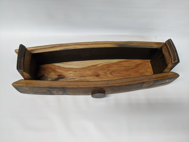 May include: A wooden serving tray made from reclaimed wine barrel staves. The tray is oval shaped and has a dark brown stain. The tray has a small wooden knob on the bottom.