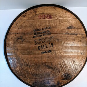 May include: A wooden barrel head with a black metal rim. The barrel head is marked with the text "JAMES B. BEAM DISTILLING CO. BOURBON WHISKEY D.-160-P.R.C. 53 D.S.P. KY. 280 C11L 19 TANK 208".