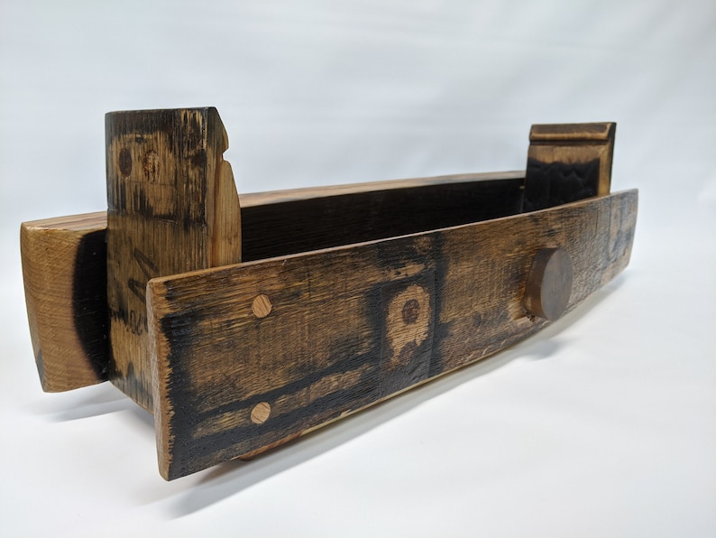 May include: A wooden shelf made from a repurposed barrel with a dark brown stain. The shelf has a rounded front edge and a small wooden knob on the right side. The shelf is made of wood with a natural grain pattern.
