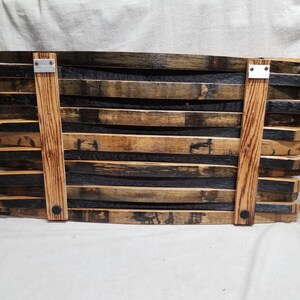 K&ouml;nnte beinhalten: Ein Wanddekor aus wiederverwendeten Holzfassdauben. Die Dauben sind versetzt angeordnet und mit Metallklammern befestigt. Das Holz hat eine nat&uuml;rliche braune und schwarze Farbe.