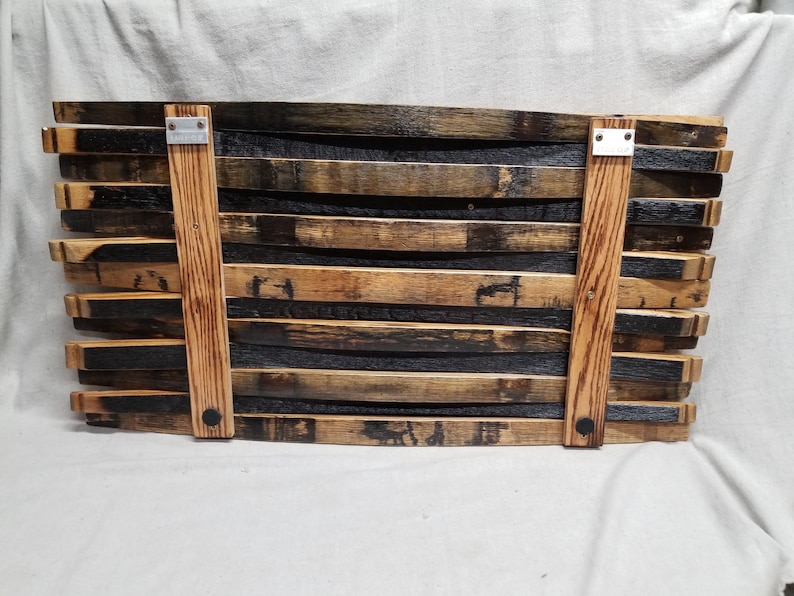 K&ouml;nnte beinhalten: Ein Wanddekor aus wiederverwendeten Holzfassdauben. Die Dauben sind versetzt angeordnet und mit Metallklammern befestigt. Das Holz hat eine nat&uuml;rliche braune und schwarze Farbe.
