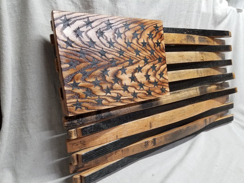 K&ouml;nnte beinhalten: Eine amerikanische Holzflagge aus wiederverwendeten Bourbon-Fassdauben. Die Sterne sind in das Holz gebrannt und die Streifen sind aus den Fassdauben gefertigt.