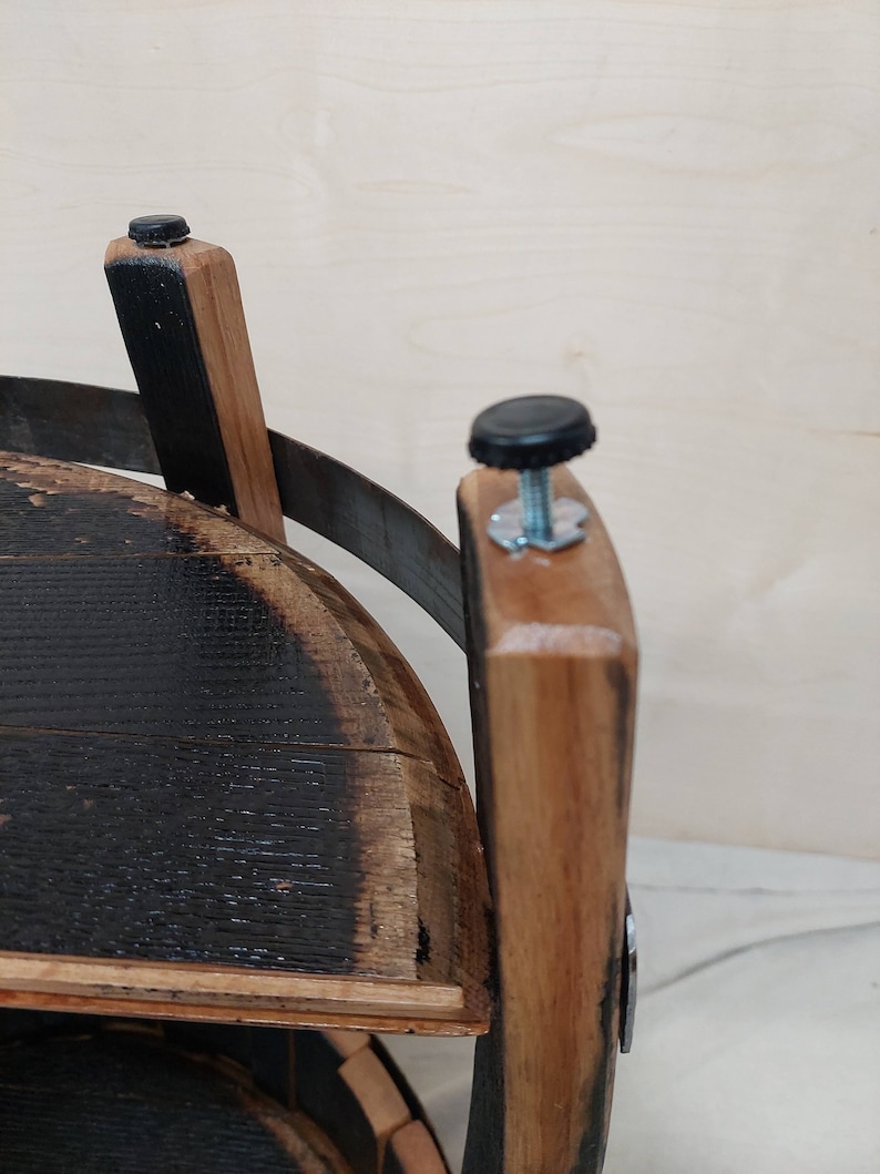K&ouml;nnte beinhalten: Eine Struktur aus Fassdauben mit einer dunkel verkohlten Innenfl&auml;che und einer nat&uuml;rlich hellbraunen Au&szlig;enseite. Das Objekt umfasst ein gebogenes Metallband und zwei verstellbare, schwarze Kunststoff-Stellf&uuml;&szlig;e mit Gewindestangen.
