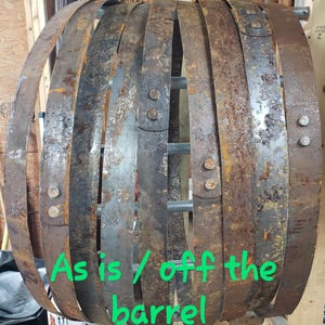 Pode incluir: Um conjunto de aros de barril de metal enferrujado e desgastado, presos por parafusos e suportes met&aacute;licos. Os aros est&atilde;o dispostos em forma circular, mostrando sinais de idade e desgaste. Texto verde: "As is / off the barrel."