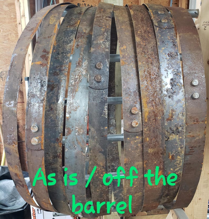 Pode incluir: Um conjunto de aros de barril de metal enferrujado e desgastado, presos por parafusos e suportes met&aacute;licos. Os aros est&atilde;o dispostos em forma circular, mostrando sinais de idade e desgaste. Texto verde: "As is / off the barrel."