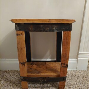May include: A small wooden end table with a single shelf. The table is made from reclaimed wood and has a rustic look. The table has a metal band around the top and bottom.