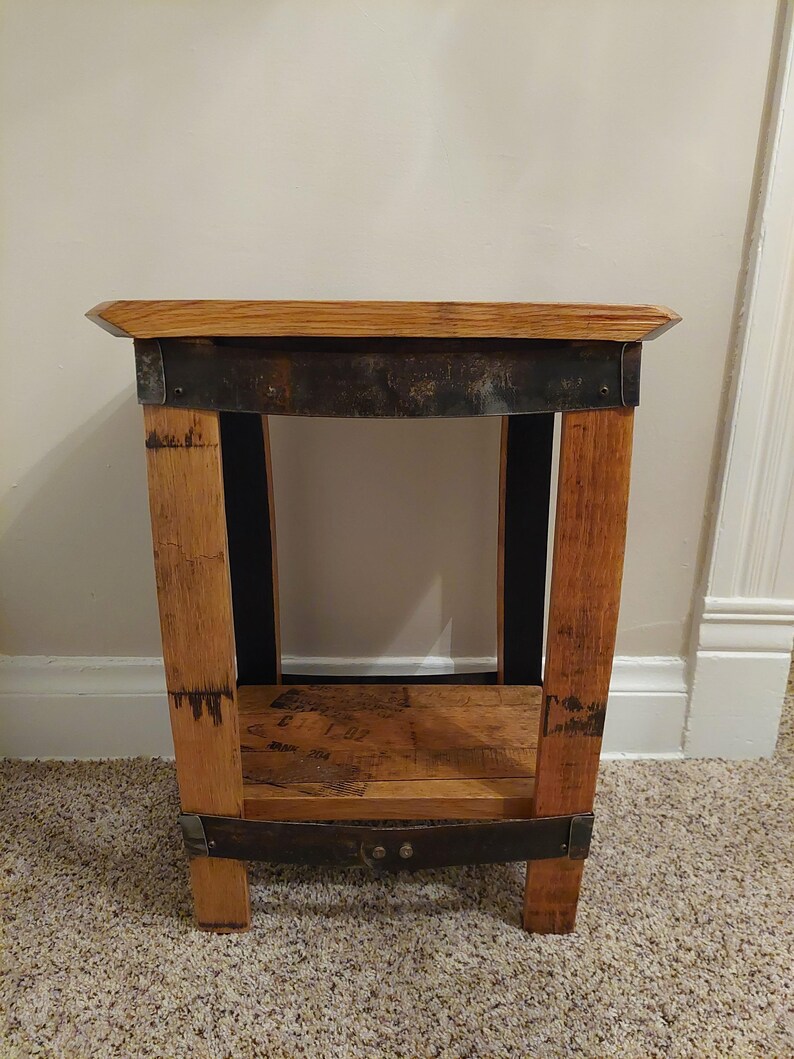 May include: A small wooden end table with a single shelf. The table is made from reclaimed wood and has a rustic look. The table has a metal band around the top and bottom.