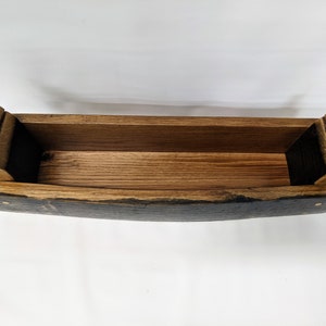 May include: A wooden planter made from a repurposed barrel stave. The planter is dark brown with a natural wood finish. It has a rectangular shape with rounded edges.