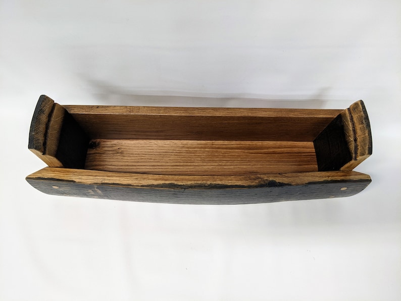May include: A wooden planter made from a repurposed barrel stave. The planter is dark brown with a natural wood finish. It has a rectangular shape with rounded edges.