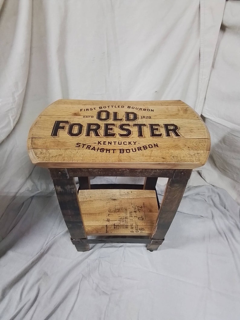 May include: A wooden side table with a top made from a reclaimed bourbon barrel. The top is branded with the words "First Bottled Bourbon", "Est. 1870", "Old Forester", "Kentucky", and "Straight Bourbon".