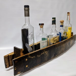 K&ouml;nnte beinhalten: Ein Flaschenhalter aus einem Holzfassdauben mit f&uuml;nf Glasflaschen. Die Flaschen sind klar und haben verschiedene Etiketten. Der Halter ist dunkelbraun mit einer nat&uuml;rlichen Holzoptik.