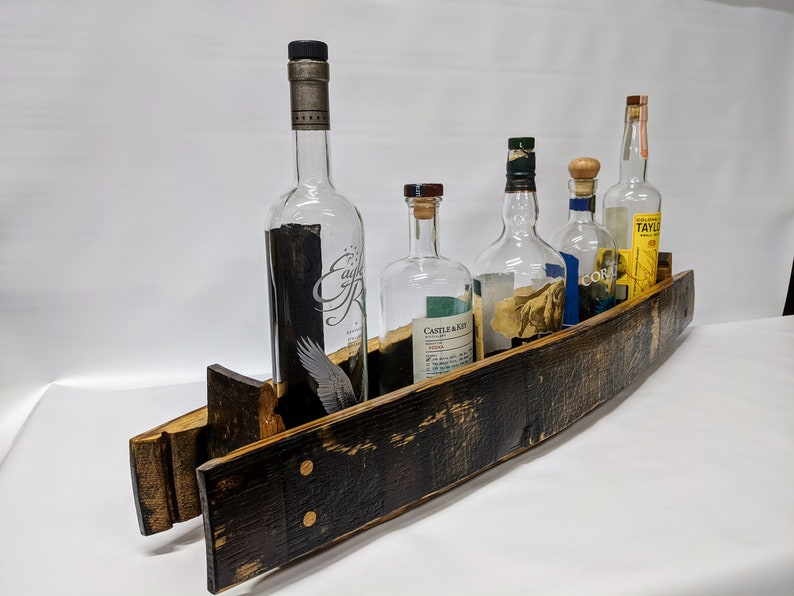 K&ouml;nnte beinhalten: Ein Flaschenhalter aus einem Holzfassdauben mit f&uuml;nf Glasflaschen. Die Flaschen sind klar und haben verschiedene Etiketten. Der Halter ist dunkelbraun mit einer nat&uuml;rlichen Holzoptik.