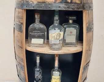 May include: A wooden barrel liquor cabinet with two shelves. The top shelf has three bottles of liquor, including Woodford Reserve, Buffalo Trace, and Disaronno. The bottom shelf has two bottles of liquor, including Eagle Rare and Colonel E.H. Taylor Jr.