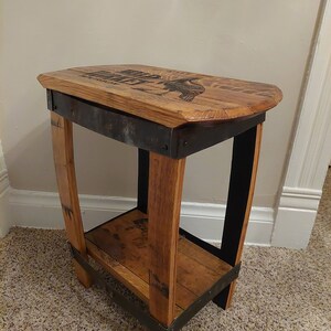 May include: A small wooden side table with a metal frame. The top of the table is made from reclaimed wood and features a design of a bird. The table has a shelf underneath.