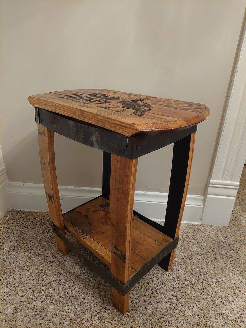 May include: A small wooden side table with a metal frame. The top of the table is made from reclaimed wood and features a design of a bird. The table has a shelf underneath.