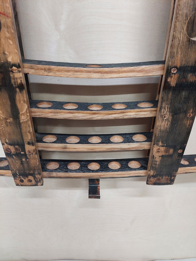 May include: A wooden wall-mounted bottle holder with three shelves. Each shelf has a row of circular holes for holding bottles. The holder is made from reclaimed wood with a dark brown stain.