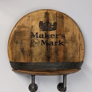 Op de afbeelding: Een houten plank gemaakt van een Maker's Mark whiskeyvat met een zwart metalen plank en twee zwarte metalen pijpbeugels.