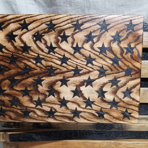K&ouml;nnte beinhalten: Eine amerikanische Holzflagge mit schwarzen Sternen, die in das Holz gebrannt wurden. Die Flagge ist aus recyceltem Holz gefertigt und hat einen rustikalen Look.