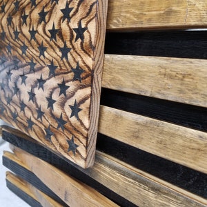 K&ouml;nnte beinhalten: Eine amerikanische Holzflagge aus recyceltem Holz mit schwarzen Sternen auf hellbraunem Hintergrund. Die Flagge wird an einer Wand gezeigt.