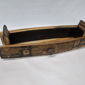May include: A wooden serving tray made from a repurposed barrel stave. The tray has a natural wood finish with dark brown char marks and a small metal knob on the front.
