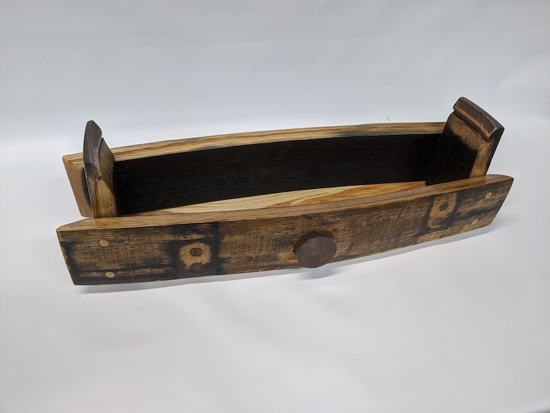 May include: A wooden serving tray made from a repurposed barrel stave. The tray has a natural wood finish with dark brown char marks and a small metal knob on the front.