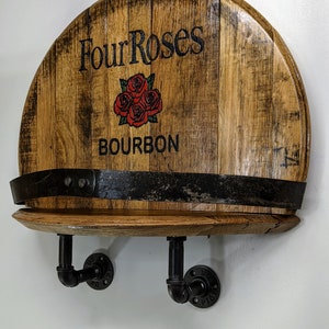 Op de afbeelding: Een houten plank gemaakt van een hergebruikt bourbonvat met het label "Four Roses Bourbon" en een zwarte metalen pijpbeugel.