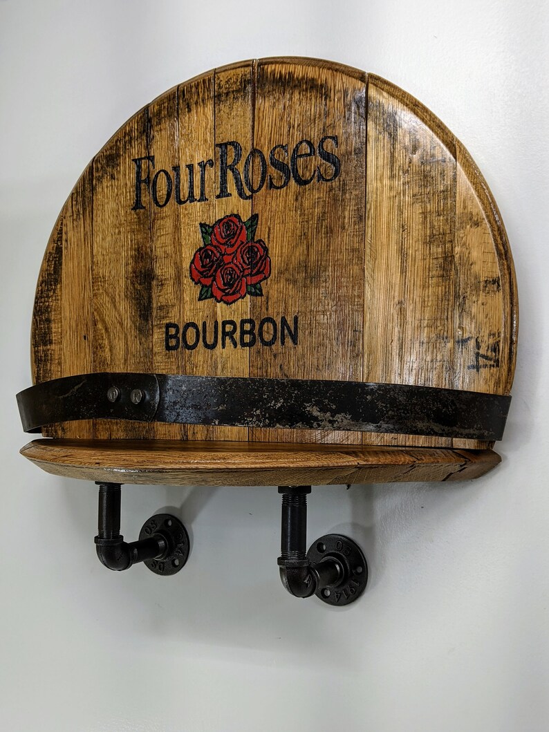 Op de afbeelding: Een houten plank gemaakt van een hergebruikt bourbonvat met het label "Four Roses Bourbon" en een zwarte metalen pijpbeugel.