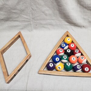 May include: A wooden triangle rack with 15 billiard balls numbered 1 through 15. The balls are arranged in a pyramid shape with the 1 ball at the top. The rack is made of light brown wood and has a dark brown stain. There is also a separate wooden diamond-shaped rack.