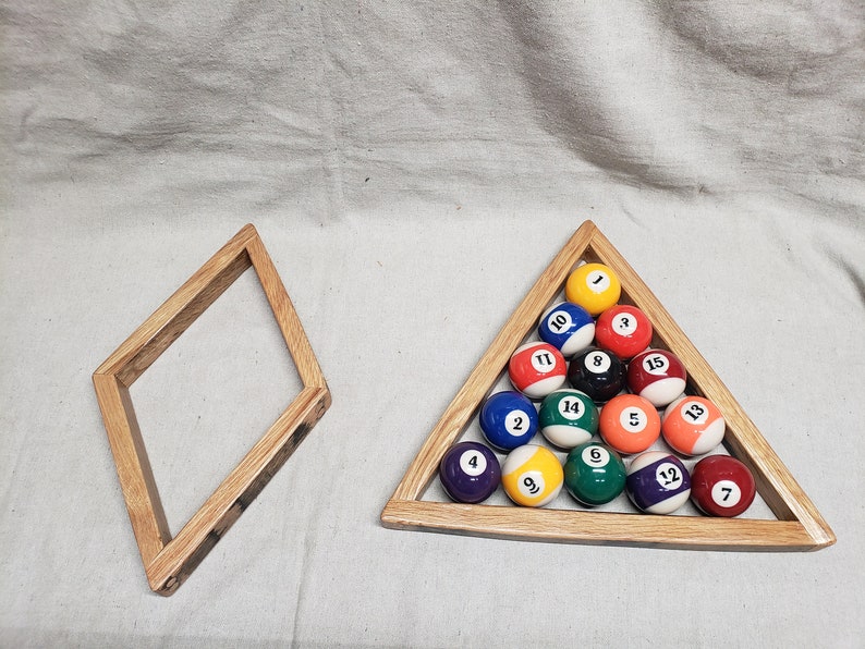 May include: A wooden triangle rack with 15 billiard balls numbered 1 through 15. The balls are arranged in a pyramid shape with the 1 ball at the top. The rack is made of light brown wood and has a dark brown stain. There is also a separate wooden diamond-shaped rack.