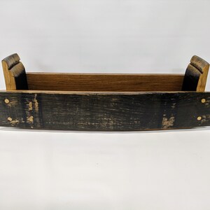 May include: A wooden tray made from a reclaimed whiskey barrel. The tray has a natural wood finish on the inside and a dark stained finish on the outside. The tray has brass accents.