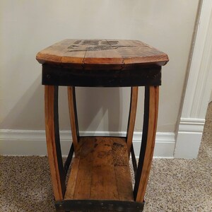 May include: A wooden end table with a single shelf, made from reclaimed wine barrels. The table has a dark brown stain and black metal accents.