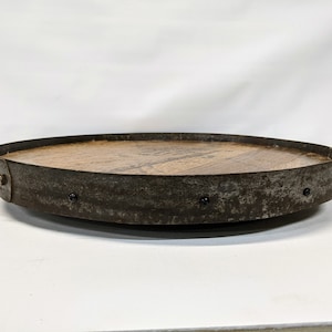 May include: A round wooden tray with a metal rim. The tray is made from reclaimed wood and has a rustic look. The metal rim is slightly rusted and has several small black rivets.