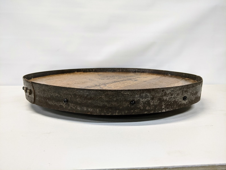 May include: A round wooden tray with a metal rim. The tray is made from reclaimed wood and has a rustic look. The metal rim is slightly rusted and has several small black rivets.