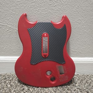 Peut inclure: Un corps de guitare électrique rouge avec une forme à double pan coupé et un pickguard à motif fibre de carbone noir. Le corps présente une découpe rectangulaire centrale, un trou pour bouton circulaire et une cavité rectangulaire plus petite.