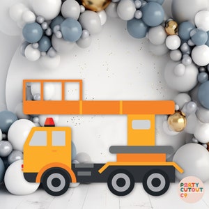 May include: A yellow construction crane cutout with a black base and orange boom. The crane is in front of a backdrop of white, gray, and silver balloons.